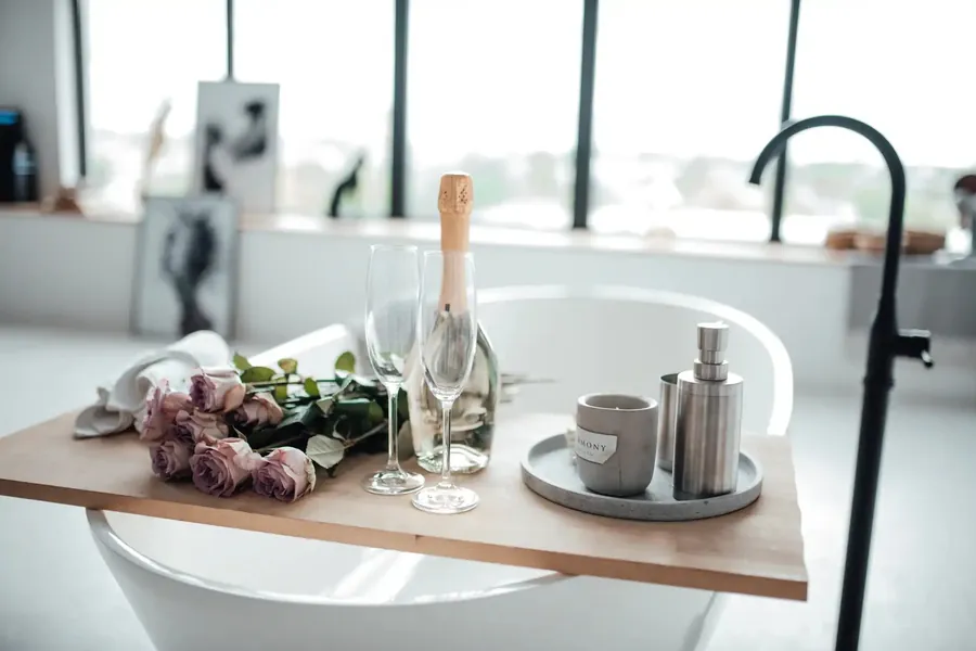 Badetablett mit Rosen, Gläsern und einer Kerze über einer freistehenden Wanne